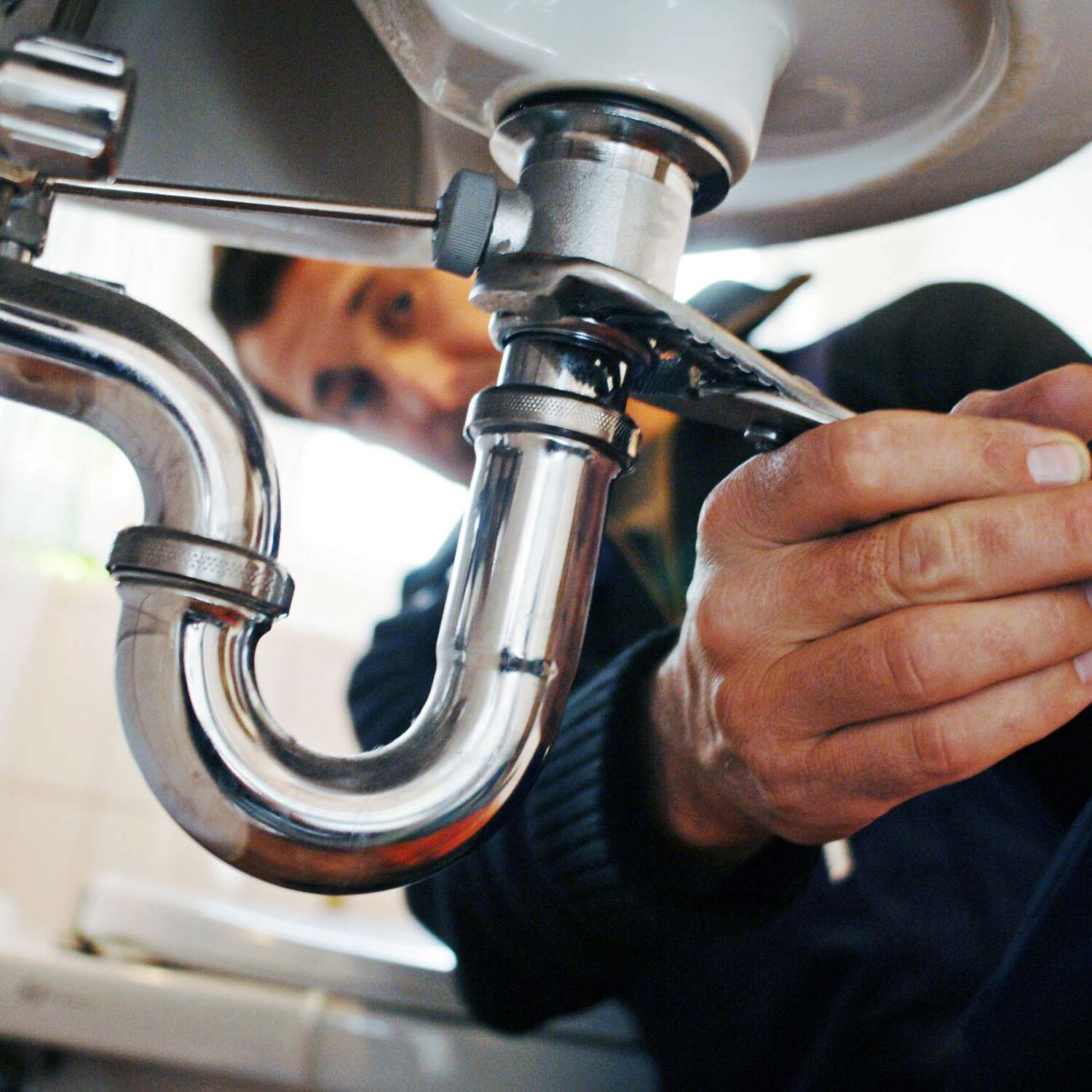 Close-up of plumber repairing sink. Male worker using tool while fixing appliance in bathroom. He is working on metallic equipment at home.